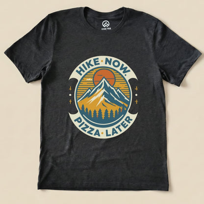 Graphic t-shirt featuring mountains, a sun, and the slogan "Hike Now Pizza Later Shirt - del" in a circular design.