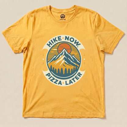 Graphic t-shirt featuring the slogan "Hike Now Pizza Later" with a mountain and sunset design on a vibrant yellow background.