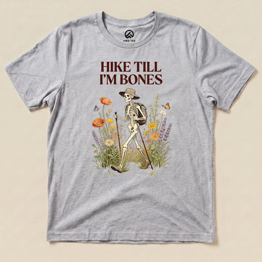 Athletic Heather Hike Till I'm Bones Shirt with a skeleton hiker walking through wildflowers graphic