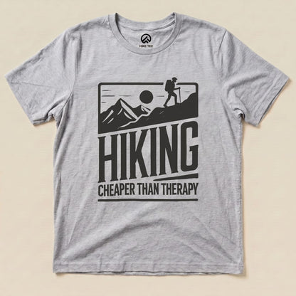 A gray graphic t-shirt features mountains, a hiker silhouette, and the slogan "Hiking Cheaper Than Therapy.