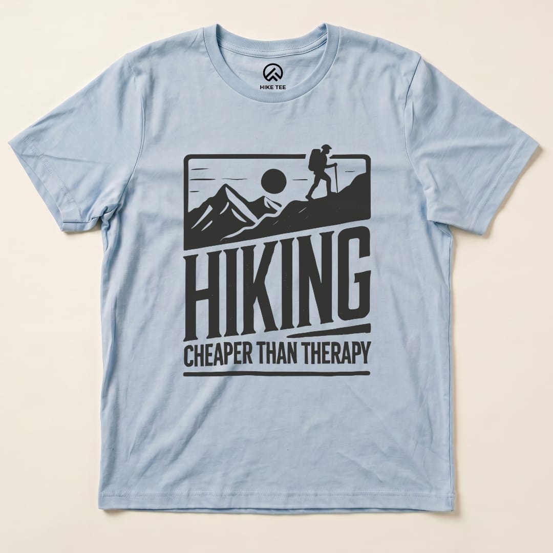 A light blue graphic t-shirt displaying the text "Hiking Cheaper Than Therapy" alongside a hiker against a mountain backdrop.