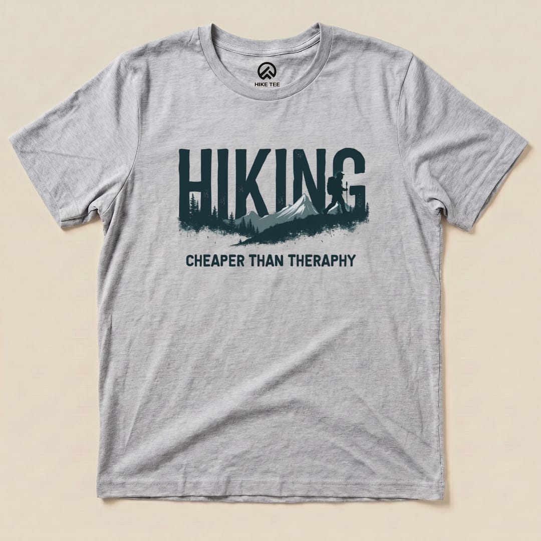 A gray graphic t-shirt featuring the slogan "Hiking - Cheaper than Therapy" alongside a mountain and forest design.