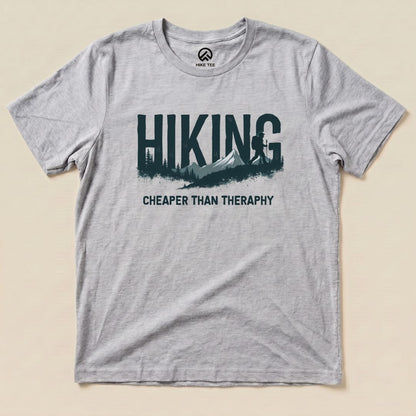 A gray graphic t-shirt featuring the slogan "Hiking - Cheaper than Therapy" alongside a mountain and forest design.