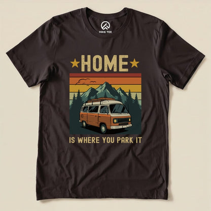 A graphic t-shirt featuring the phrase "HOME IS WHERE YOU PARK IT" alongside an illustration of a vintage camper van against mountains.