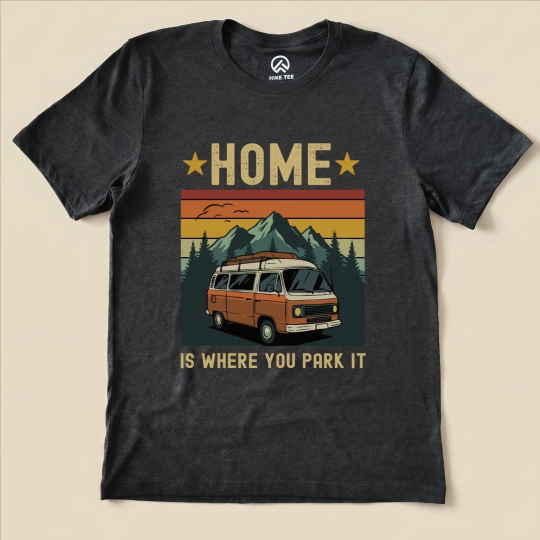 A graphic t-shirt featuring the phrase "HOME IS WHERE YOU PARK IT" above an illustration of a vintage camper van and mountains.