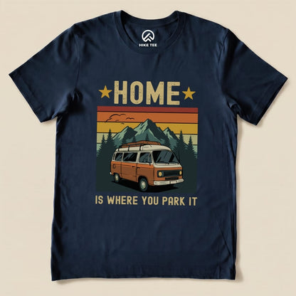 A graphic t-shirt featuring an orange van surrounded by mountains and trees, with the phrase "Home Is Where You Park It" prominently displayed.