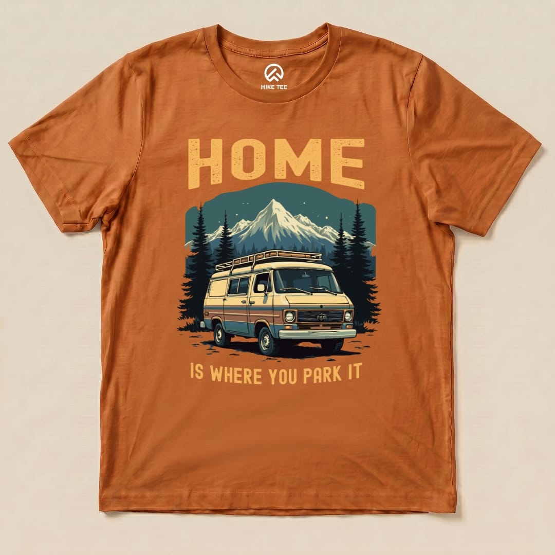 The "Home You Park It Shirt" features a graphic of a vintage camper van with mountains and trees, printed on an orange t-shirt.