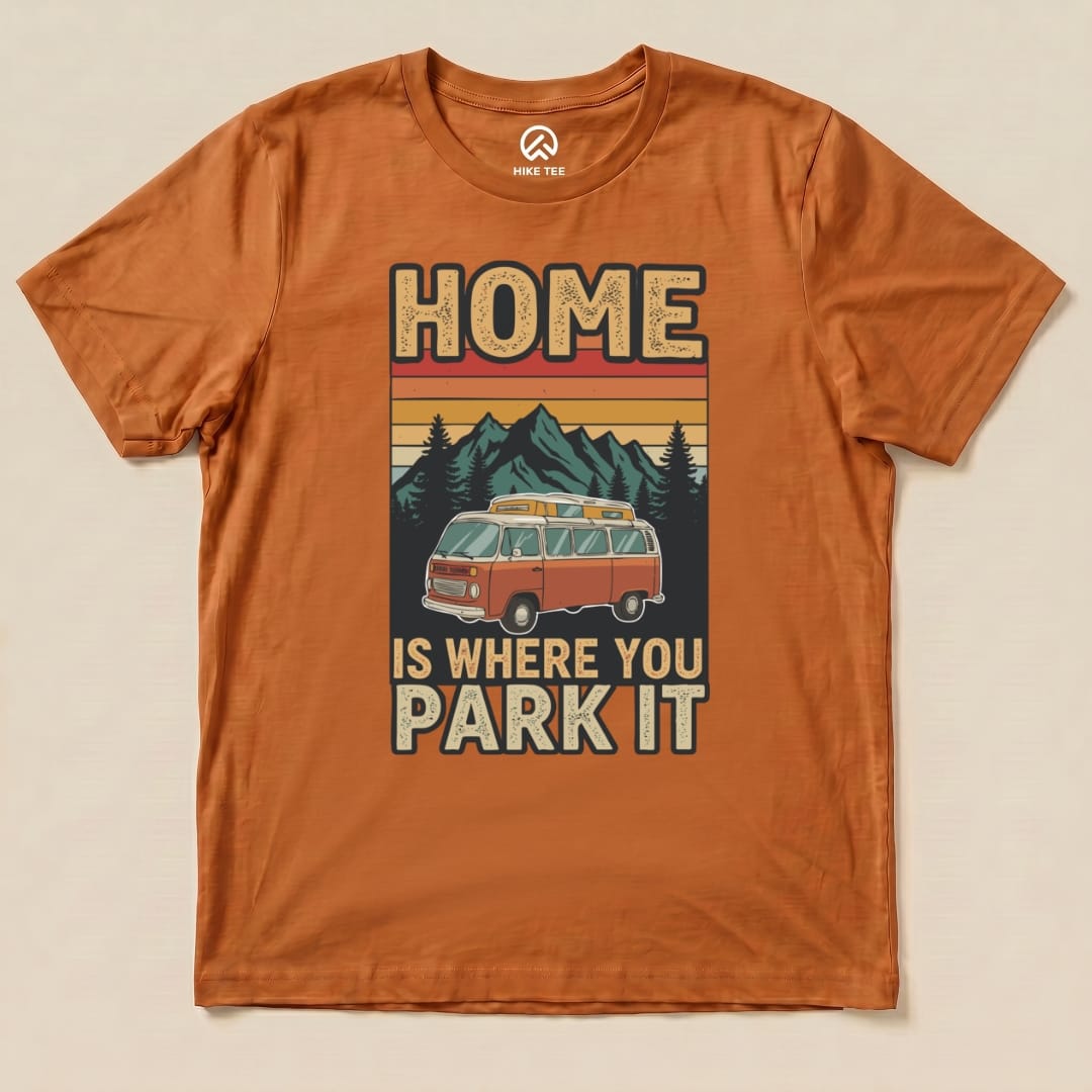The orange graphic t-shirt features a retro design with the phrase "HOME IS WHERE YOU PARK IT" and an illustration of a vintage camper van against a mountain backdrop.
