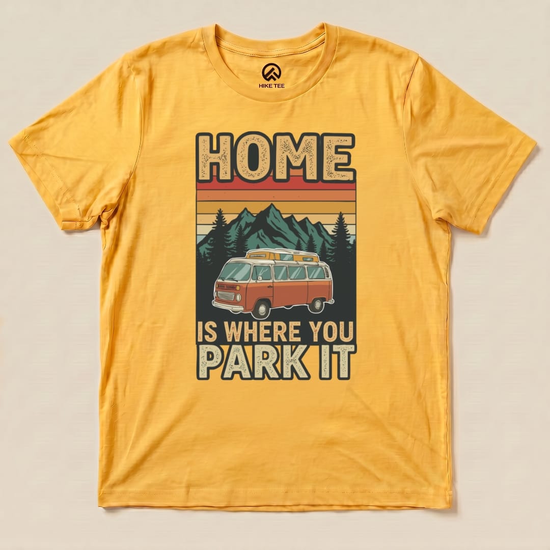 A graphic t-shirt in vibrant yellow featuring a retro van and the slogan "HOME IS WHERE YOU PARK IT" against mountains.