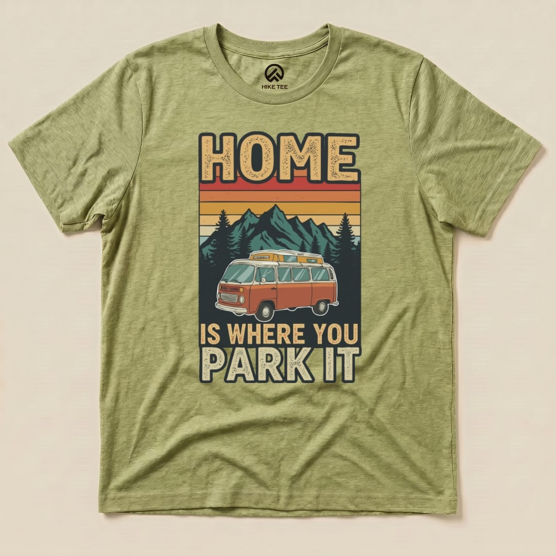 A graphic t-shirt in an olive green color featuring the phrase "Home is Where You Park It" alongside a vintage orange van and mountains.