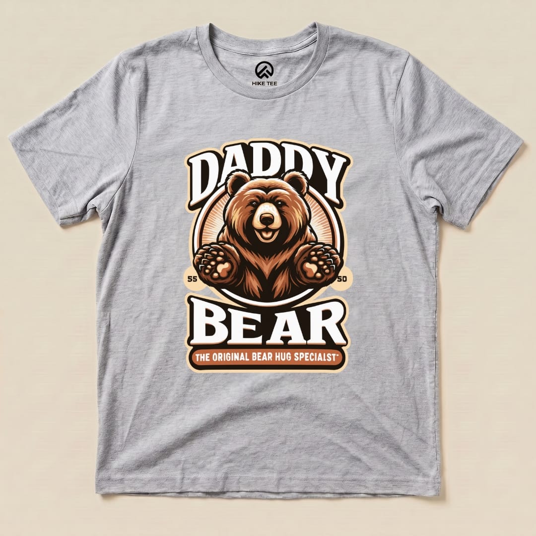 A graphic t-shirt featuring a stylized bear and the slogan "Daddy Bear" with "The Original Bear Hug Specialist" below it, in earthy colors.