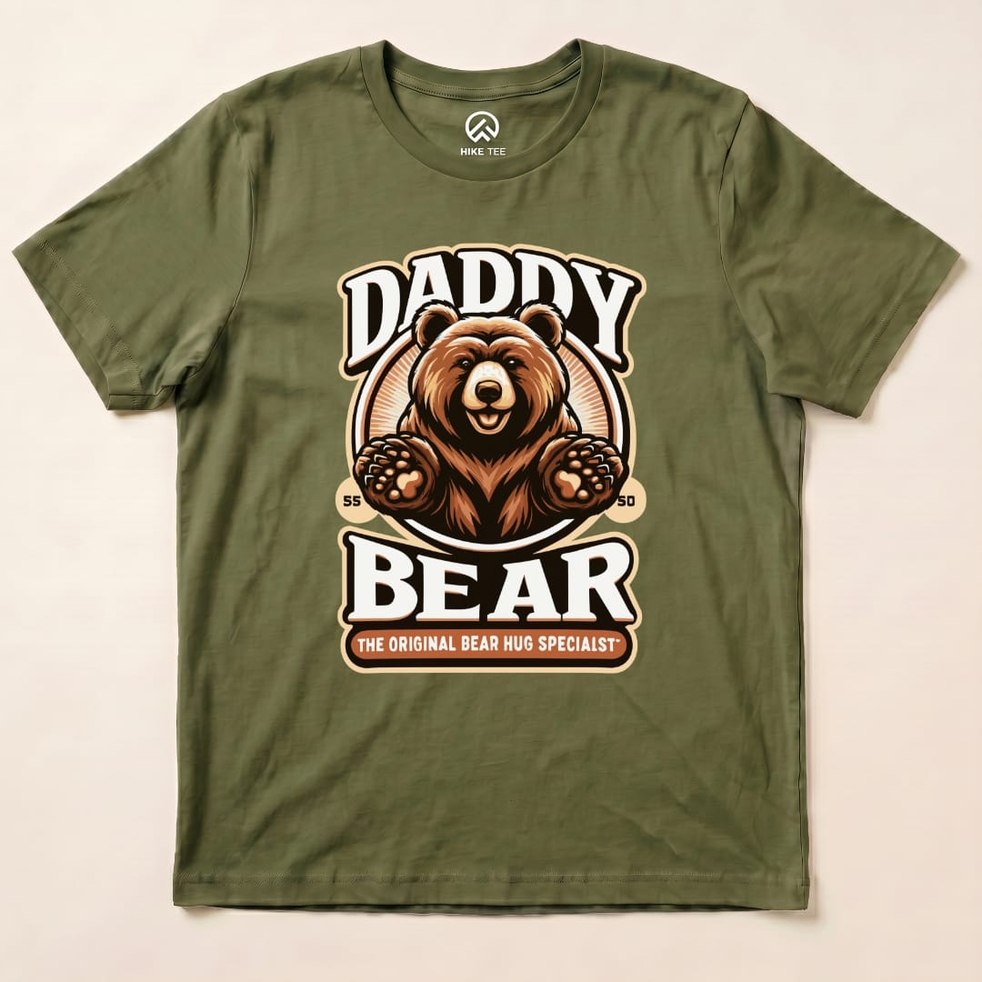 A graphic t-shirt featuring a friendly bear with the text "Daddy Bear" and "The Original Bear Hug Specialist," in earthy tones.