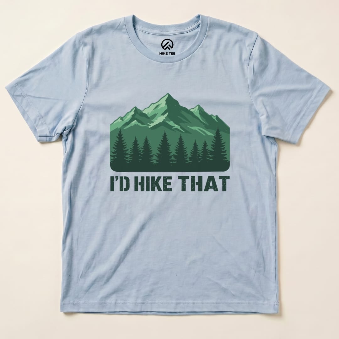 A light blue graphic t-shirt featuring a mountain scene with evergreen trees and the text "I'D HIKE THAT" printed below.