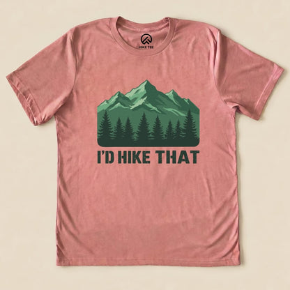 A flat lay of a pink graphic t-shirt featuring a mountain design and the text "I'D HIKE THAT" printed in bold letters.