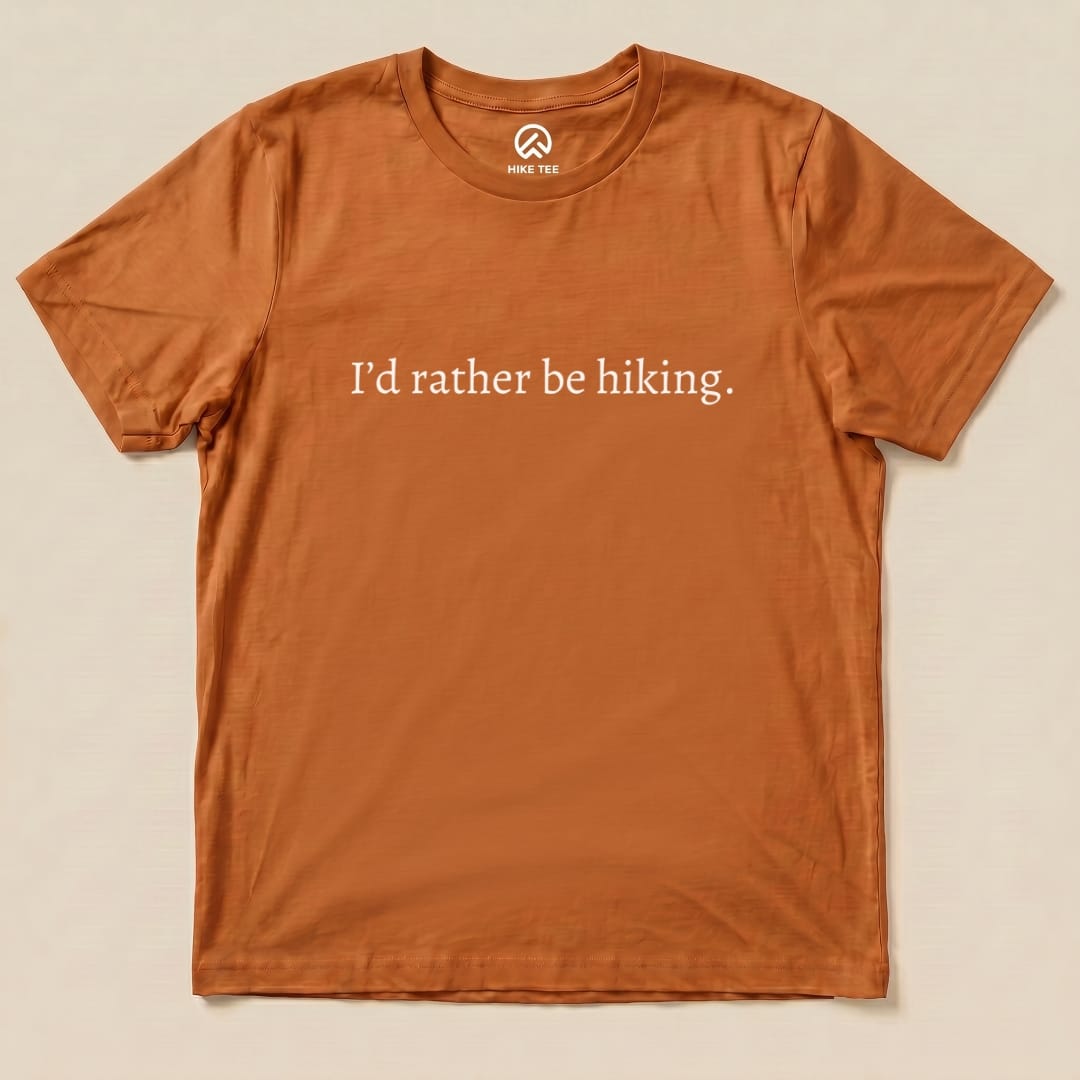 A flat, orange graphic t-shirt featuring the slogan "I'd rather be hiking." printed boldly across the front.