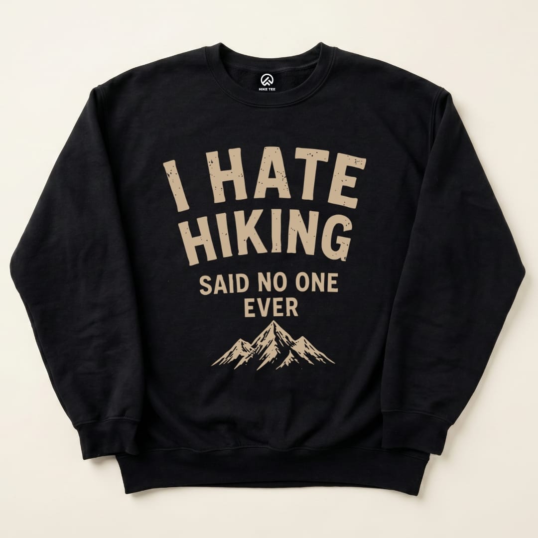 A "I Hate Hiking Sweatshirt" in black features bold beige lettering that reads, "I HATE HIKING SAID NO ONE EVER," above a mountain graphic.
