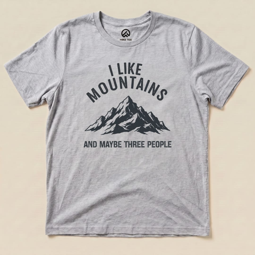 A gray graphic t-shirt featuring the text "I Like Mountains" above a mountain graphic, with the phrase "AND MAYBE THREE PEOPLE" below.