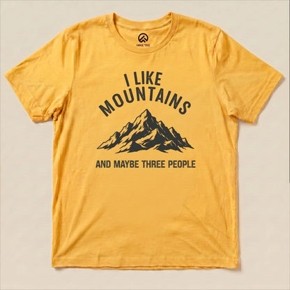 A graphic t-shirt featuring a mountain illustration with the text "I Like Mountains AND MAYBE THREE PEOPLE" in a bold design.