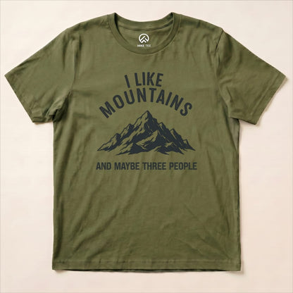 A graphic t-shirt in olive green featuring the slogan "I Like Mountains" above a mountain design with "AND MAYBE THREE PEOPLE.