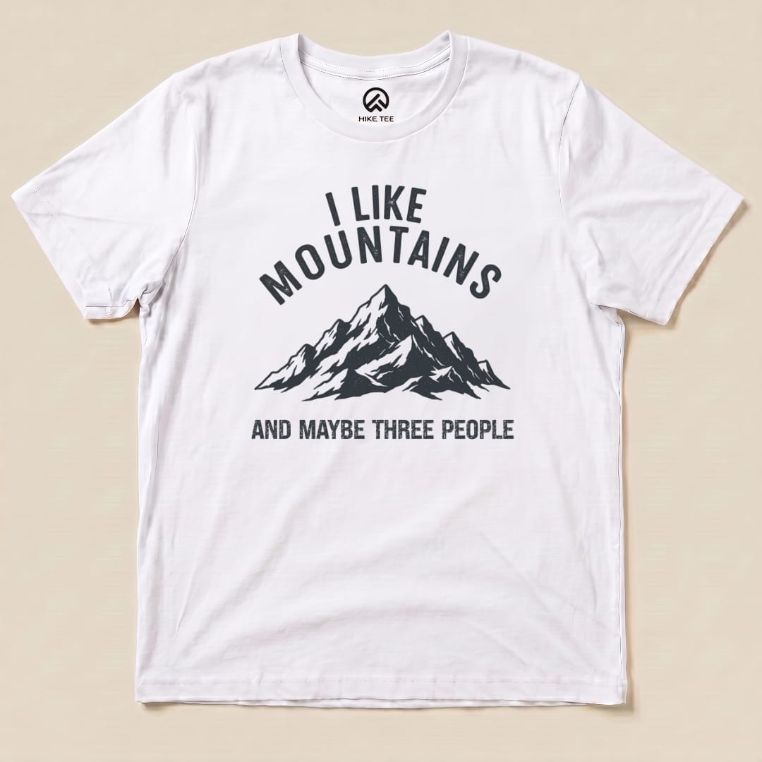 A white graphic t-shirt featuring a black mountain design and the text "I Like Mountains AND MAYBE THREE PEOPLE.