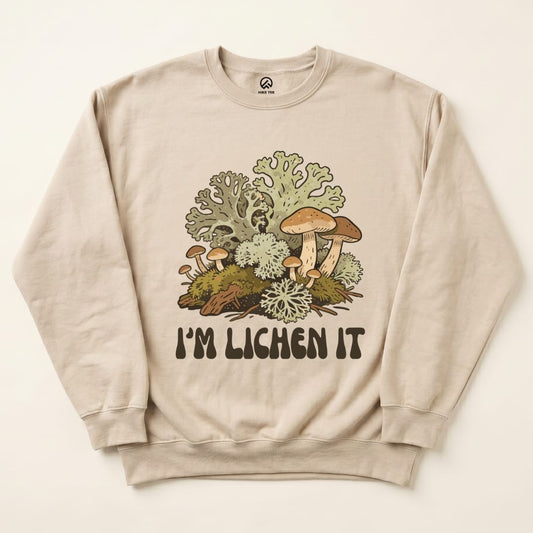 A beige sweatshirt featuring the graphic "I'm Lichen It" with colorful mushrooms and lichen designs on the front.