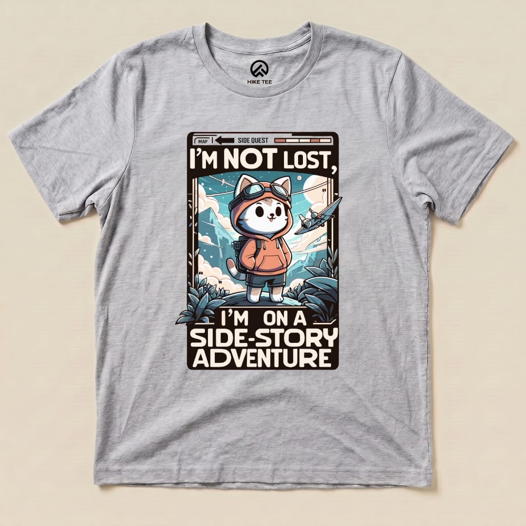 Gray graphic t-shirt featuring a cartoon cat in a hoodie with goggles, stating "I'm Not Lost, I'm on a Side-Story Adventure.