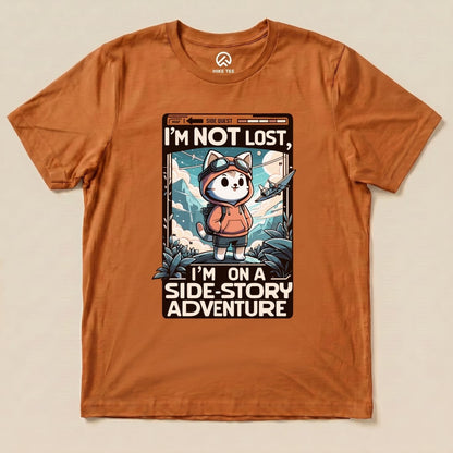 A graphic t-shirt in orange features a whimsical design of a cat in an explorer outfit with the text "I'm Not Lost, I'm on a Side-Story Adventure.