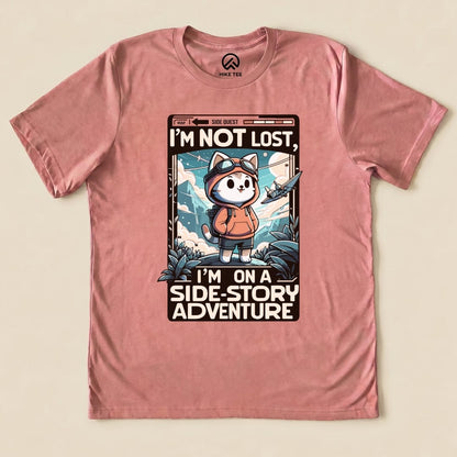 Graphic t-shirt featuring a playful cat in a hiking outfit and the text, "I'm Not Lost, I'm on a Side-Story Adventure.