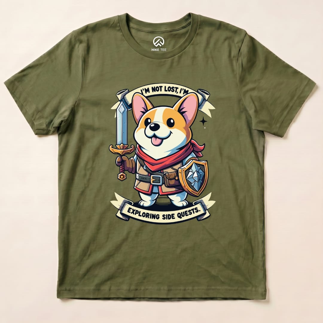 The olive green graphic t-shirt features a cheerful corgi holding a sword and shield, with the words "I'm Not Lost, I'm Exploring Side Quests" printed above and below.