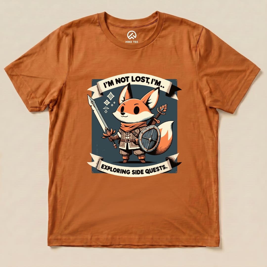 The "I'm Not Lost Fox Shirt" features a charming fox character holding a sword and shield with the slogan “I’m not lost, I’m exploring side quests” printed on an orange graphic t-shirt.