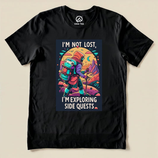 A black graphic t-shirt featuring the slogan "I'm Not Lost, I'm Exploring Side Quests" with a colorful illustration of a hiker amidst a vibrant landscape.