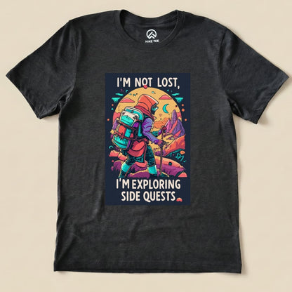 A black graphic t-shirt features the phrase "I'M NOT LOST, I'M EXPLORING SIDE QUESTS" alongside a backpacker exploring a vibrant landscape.