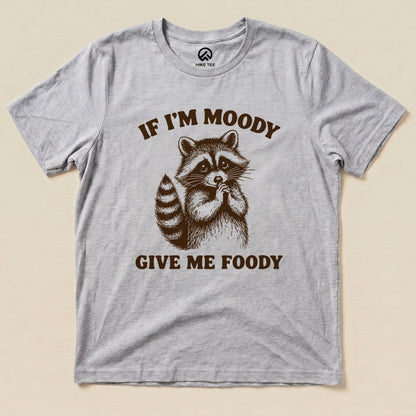 A gray graphic t-shirt features an illustration of a raccoon with the text "IF I'M MOODY GIVE ME FOODY" below it.