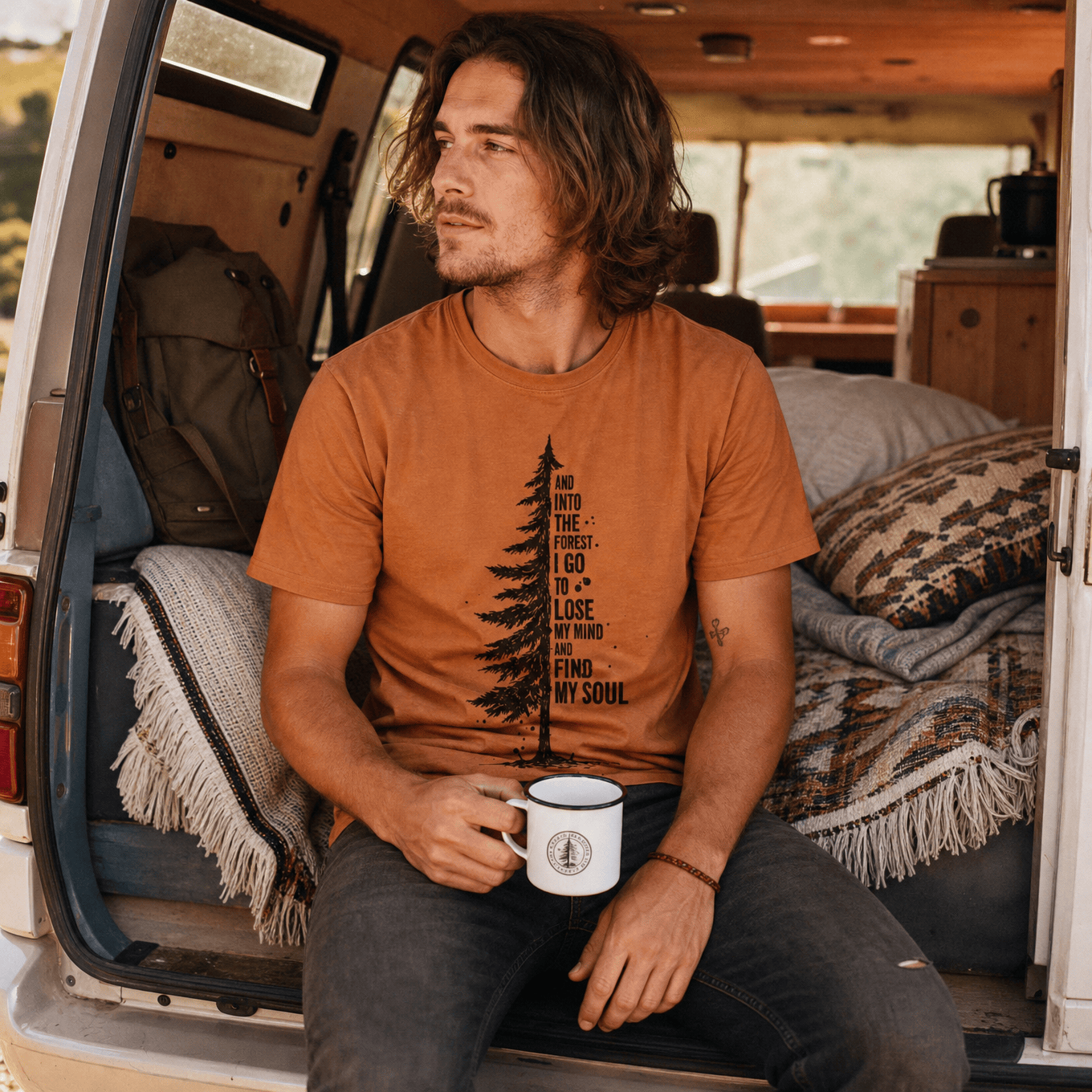A man sits in the back of a van, wearing an "In The Forest Shirt" featuring a tree graphic and the phrase about finding one's soul.