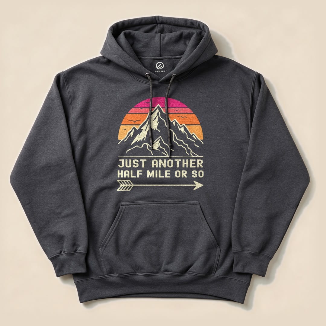 A charcoal gray hoodie featuring a graphic design of mountains and a sunset, with the phrase "JUST ANOTHER HALF MILE OR SO.