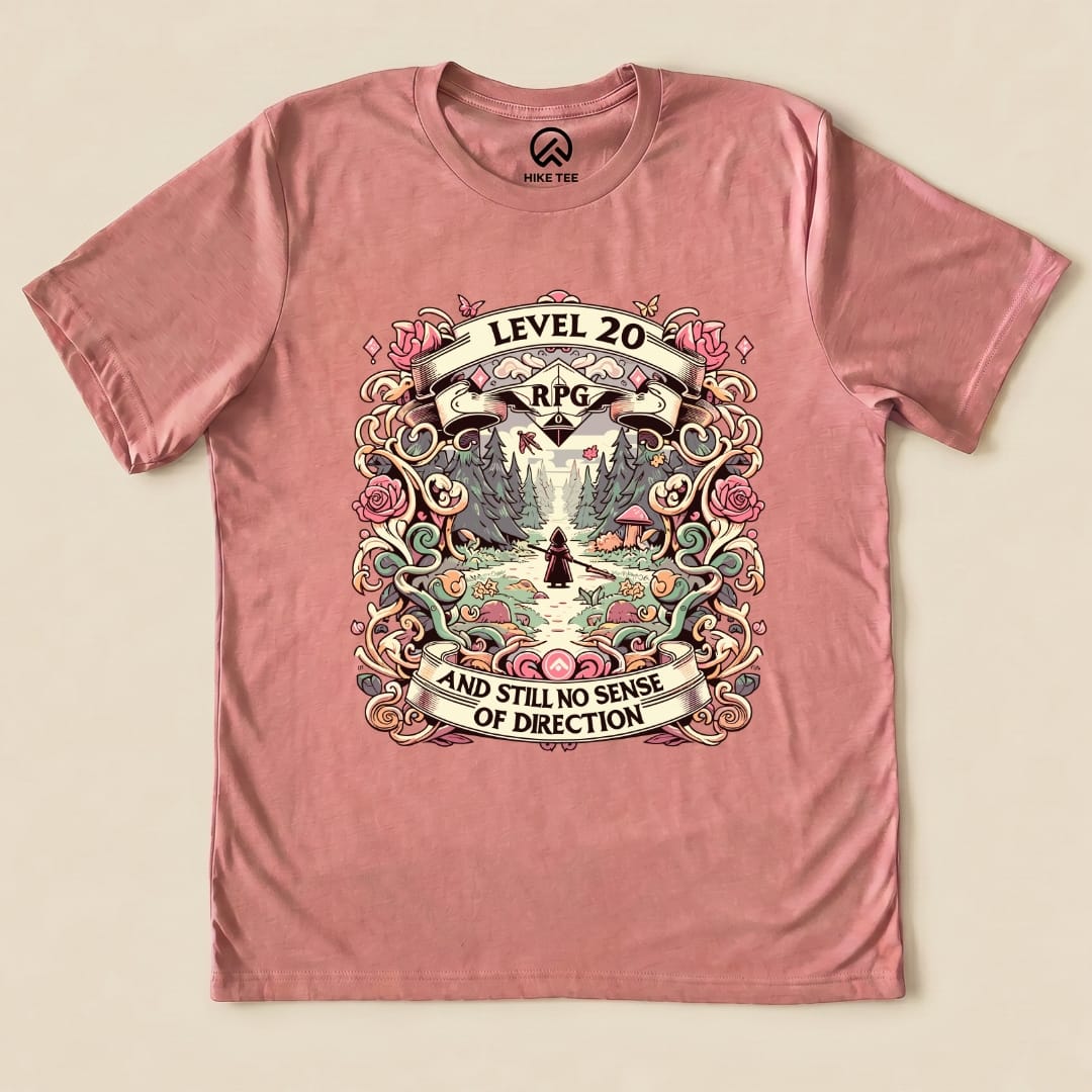 Graphic t-shirt featuring a whimsical design with "Level 20 RPG" and the slogan "AND STILL NO SENSE OF DIRECTION" on a pink background.