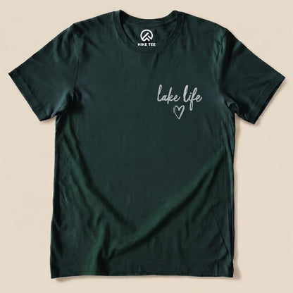 A graphic t-shirt in dark green featuring the phrase "lake life" with a heart design, part of the Like Life Shirt collection.