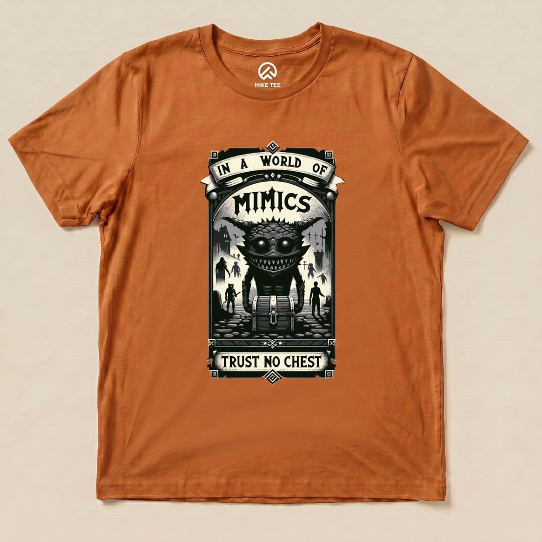 The orange graphic t-shirt features the "Mimics Shirt" design, showcasing a large monster with the slogan "In a World of Mimics, Trust No Chest.