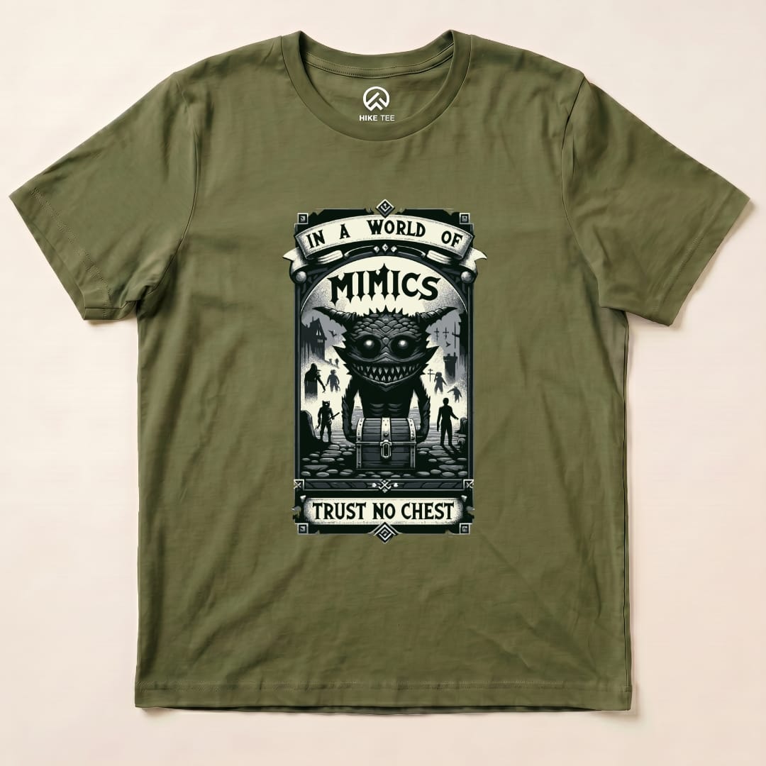 A flat olive green graphic t-shirt features a design with the words "In a World of Mimics" and a creature beside a treasure chest, saying "Trust No Chest.