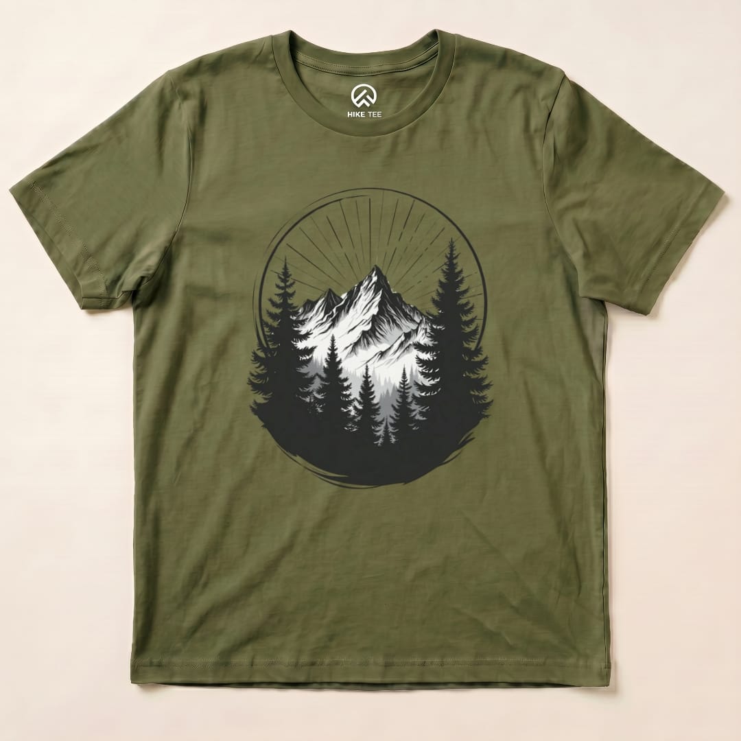 The Monochrome Mountains Shirt features a striking graphic of snowy peaks surrounded by dark trees, set against an olive green background.