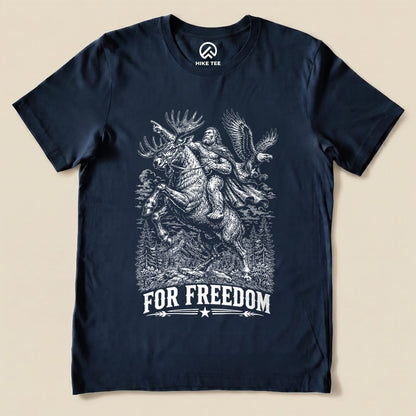 A navy graphic t-shirt features a comical design of Bigfoot riding a moose beneath the slogan "FOR FREEDOM".