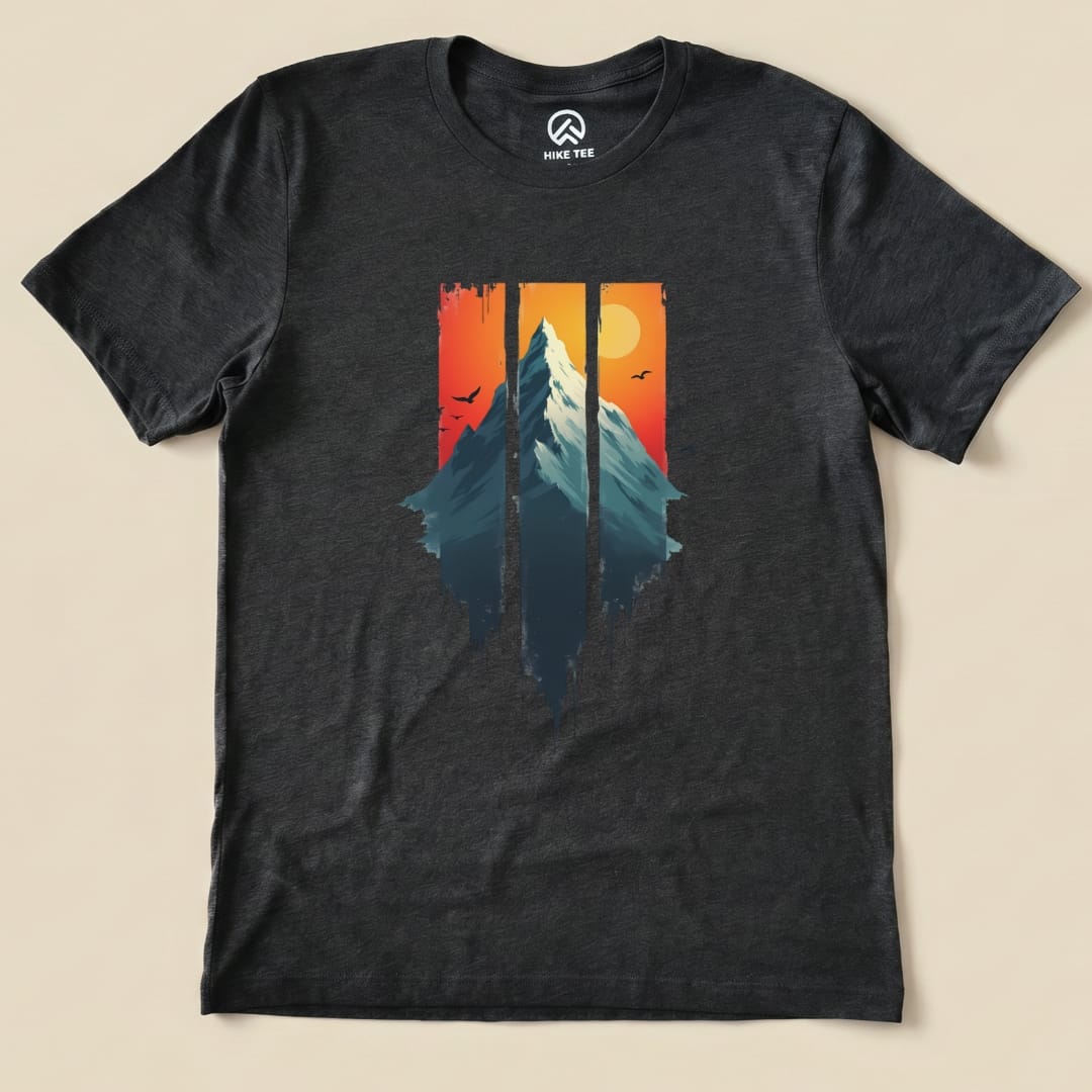 The Mountain Sunset Shirt features a graphic of a mountain silhouette against a vibrant sunset with birds flying in the background.