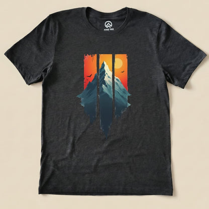 The Mountain Sunset Shirt features a graphic of a mountain silhouette against a vibrant sunset with birds flying in the background.