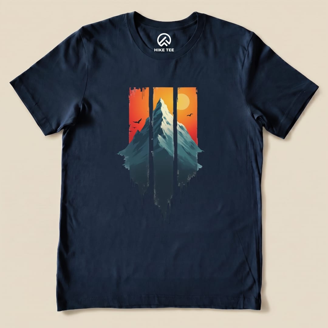 The Mountain Sunset Shirt features a graphic of a snow-capped mountain against a sunset backdrop with silhouettes of trees and birds.