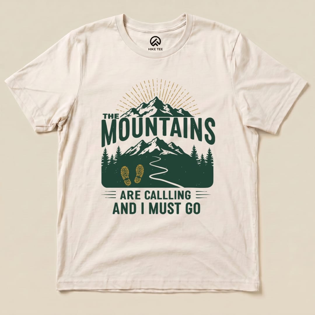 Graphic t-shirt featuring green text "THE MOUNTAINS ARE CALLING AND I MUST GO" above a mountain and hiking design.