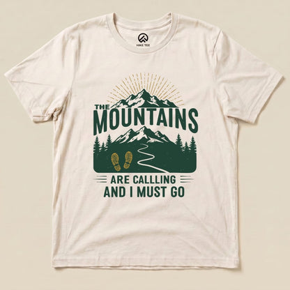 Graphic t-shirt featuring green text "THE MOUNTAINS ARE CALLING AND I MUST GO" above a mountain and hiking design.