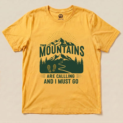 Graphic t-shirt featuring the text "THE MOUNTAINS ARE CALLING AND I MUST GO" with a mountain scene and footprints, on a yellow background.