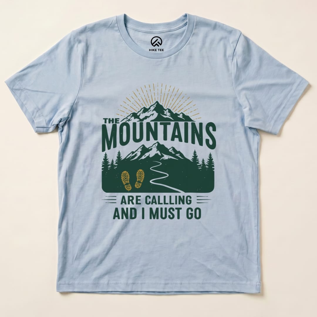 The "Mountains Are Calling Shirt" features a scenic graphic of mountains, trees, and a path, printed on a light blue graphic t-shirt.