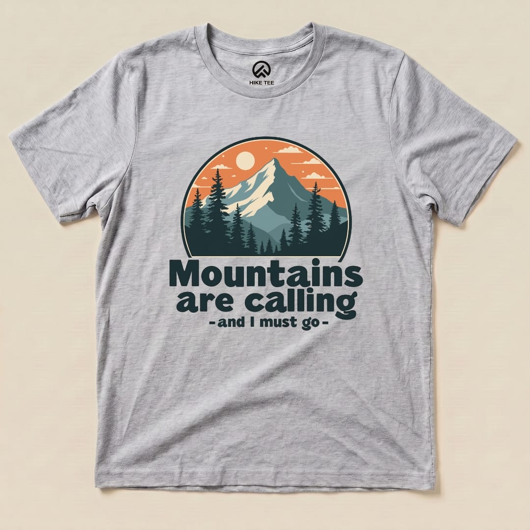 A graphic t-shirt featuring an illustrated mountain scene with the text "Mountains are calling - and I must go" prominently displayed.