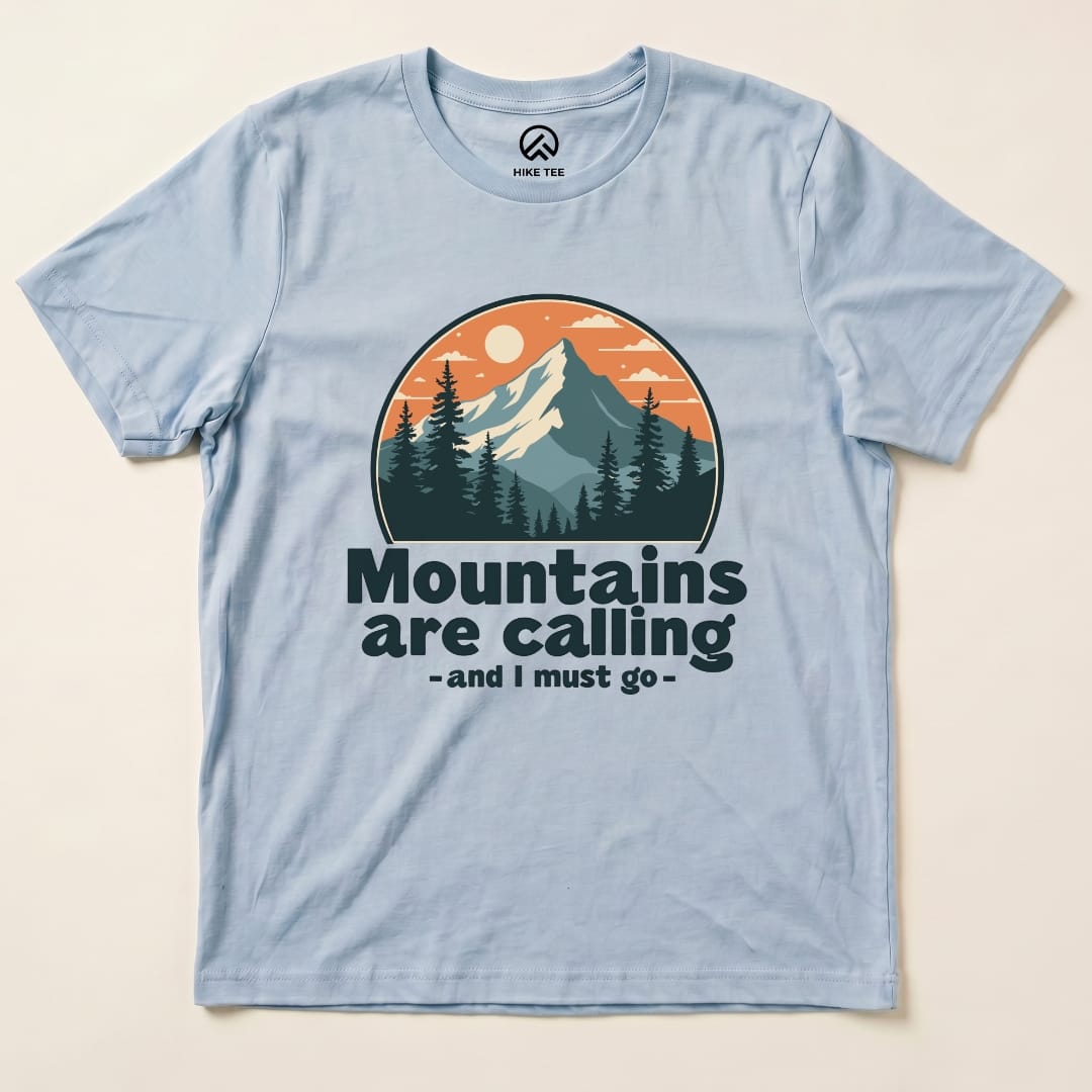 Light blue graphic t-shirt featuring the slogan "Mountains are calling - and I must go" with a mountain and sunset design.